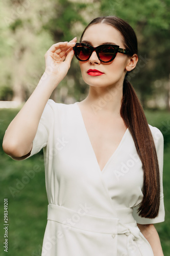 portrait of young woman in sunglasses. The girl in the white dress. Walk in the Park. Long-haired brunette. Female portrait. Young woman wearing sunglasses.