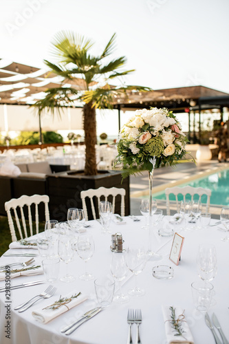 White table setting with floral centerpiece at outdoors wedding reception. © Drazen