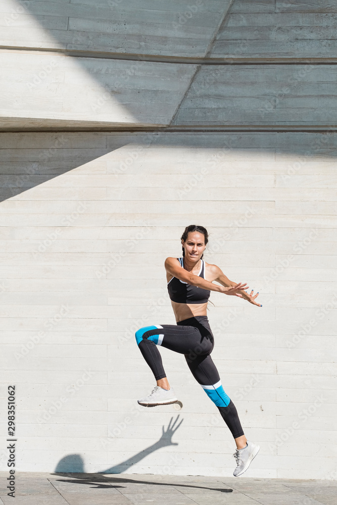 Full body of female athlete in sportswear jumping on concrete Full body of female athlete in sportswear jumping on concrete