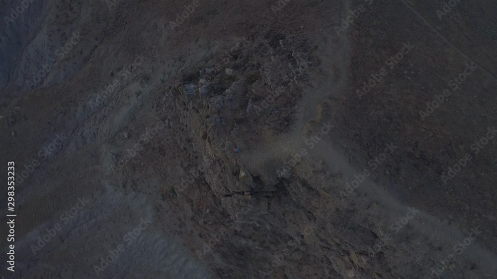 Aerial view girl sitting in the mountains near the cliff and takes pictures om mobile phone. Evening time after sunset Aerial view girl sitting in the mountains near the cliff and takes pictures om mobile phone. Evening time after sunset