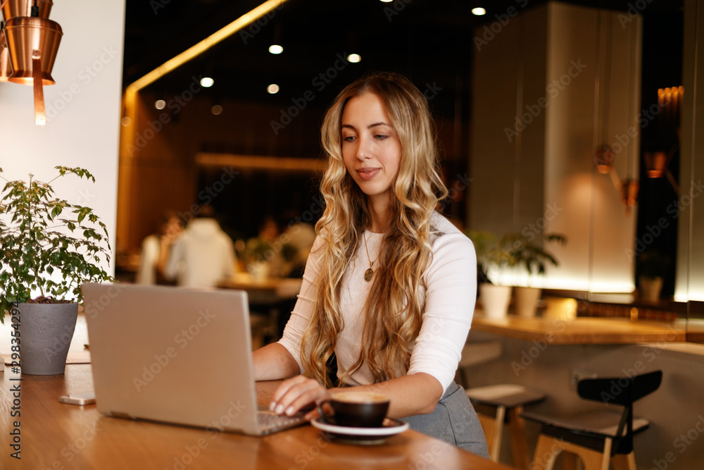 Technology. Work. Freelance. Young woman is working with her laptop and smiling while sitting in cafe Technology. Work. Freelance. Young woman is working with her laptop and smiling while sitting in cafe