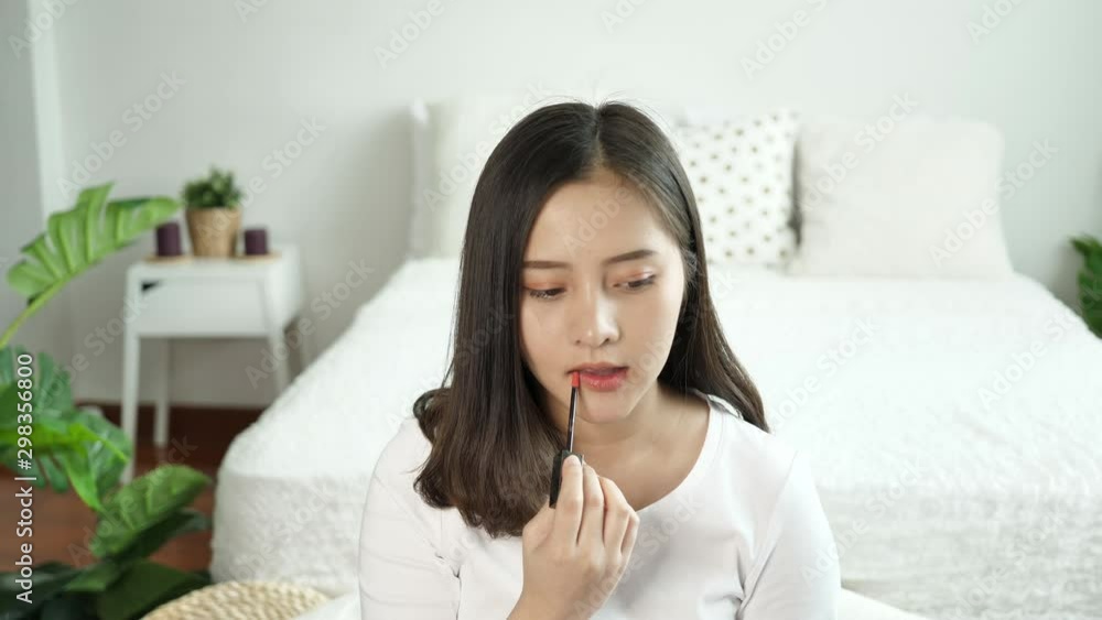 Asian woman makes makeup oneself. Young woman makeup with lipstick at lips sitting in the bedroom in the morning there was sunshine from the window. Beauty makeup concept. Slow motion Asian woman makes makeup oneself. Young woman makeup with lipstick at lips sitting in the bedroom in the morning there was sunshine from the window. Beauty makeup concept. Slow motion