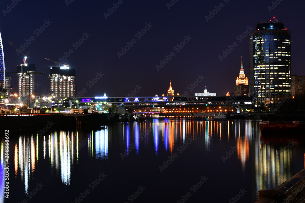 Fototapeta premium brightly lit tall buildings at night and reflected in the river