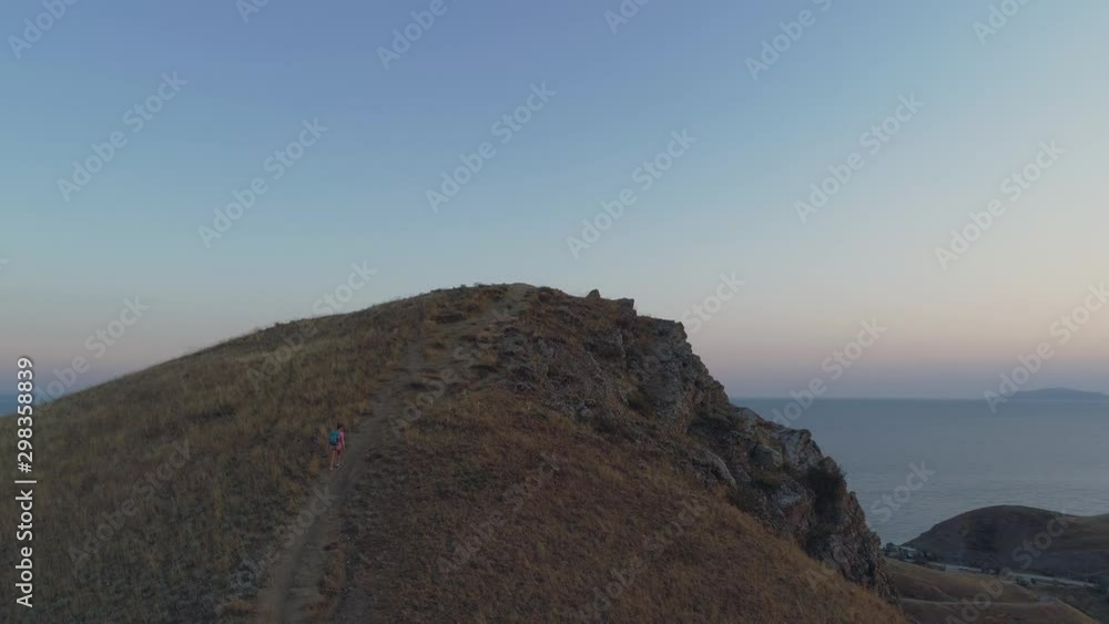 Aerial view girl with backpack rises up to mountain during sunset. Flight around. City in a background. Aerial view girl with backpack rises up to mountain during sunset. Flight around. City in a background.
