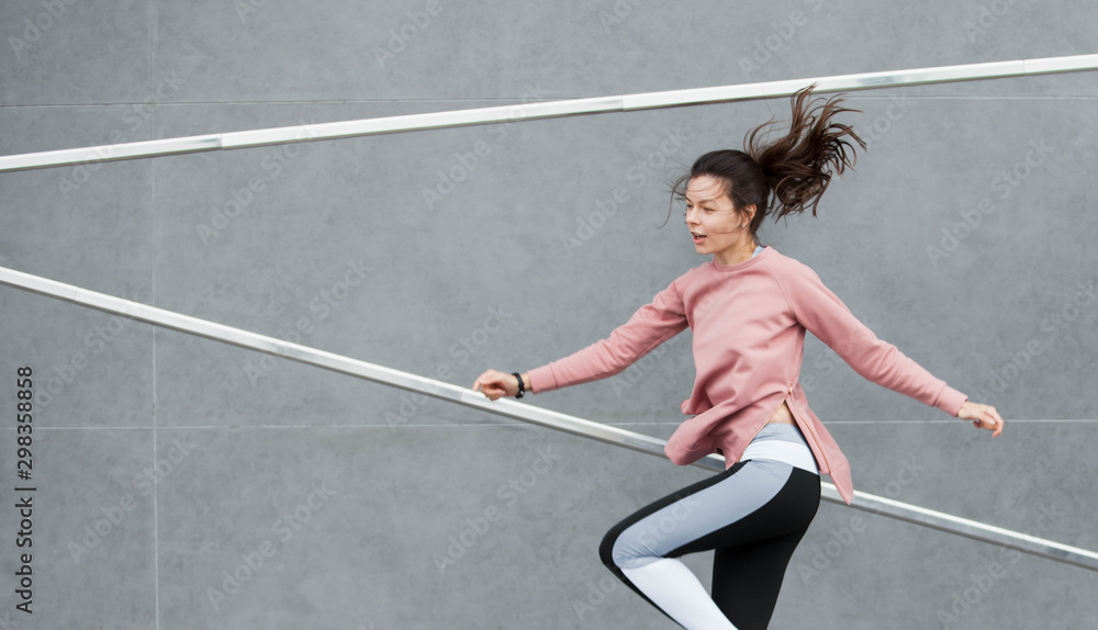 An athletic young woman is jumping, doing acrobatics, ballet, is actively involved in sports, against a concrete wall.