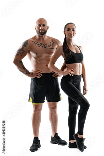 Athletic man in black shorts and sneakers with brunette woman in leggings and top posing isolated on white background. Fitness couple, gym concept. © nazarovsergey