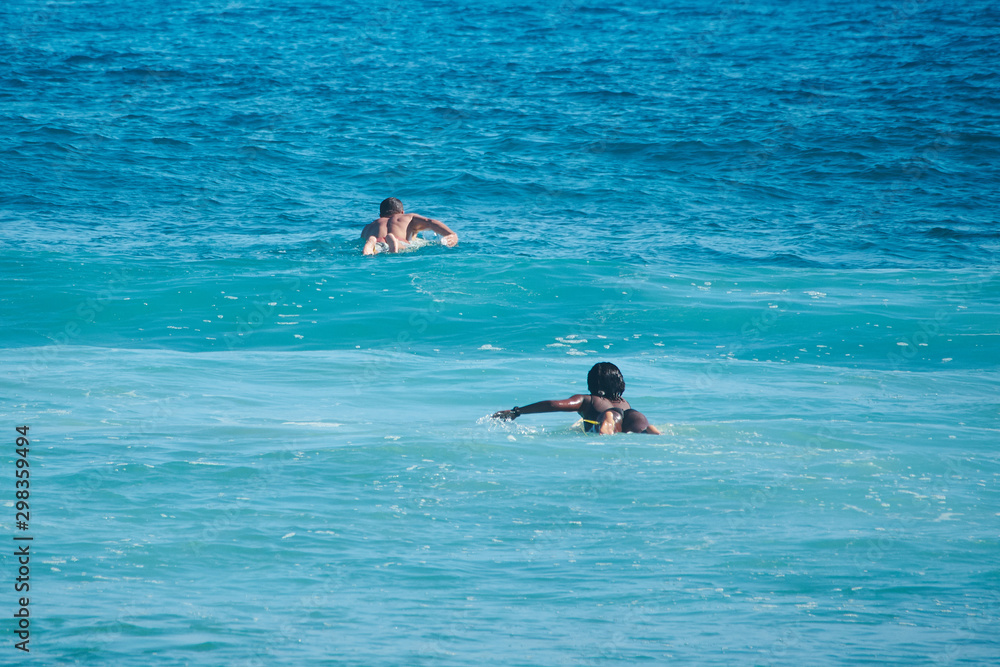 White man and black woman surfers swim on line up. Back view. Lifestule.