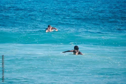 White man and black woman surfers swim on line up. Back view. Lifestule.