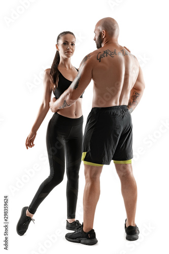 Athletic man in black shorts and sneakers with brunette woman in leggings and top posing isolated on white background. Fitness couple  gym concept.