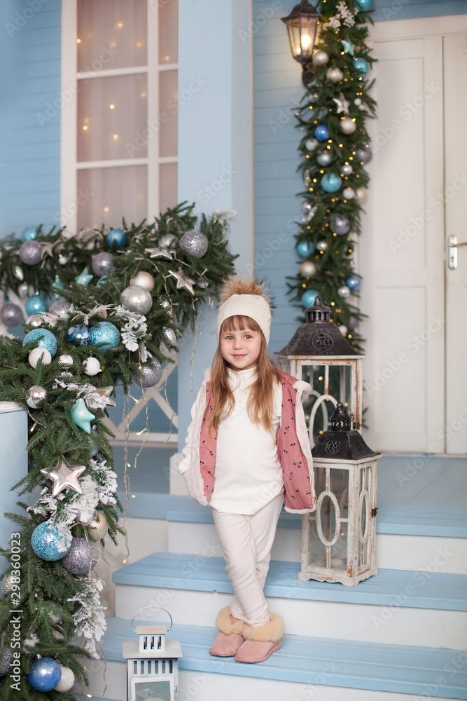 Merry Christmas, happy holidays! New Year 2020. little girl stands on porch of house decorated for Christmas. child decorates terrace for new year. Christmas decorated outdoor terrace with garlands. Merry Christmas, happy holidays! New Year 2020. little girl stands on porch of house decorated for Christmas. child decorates terrace for new year. Christmas decorated outdoor terrace with garlands.