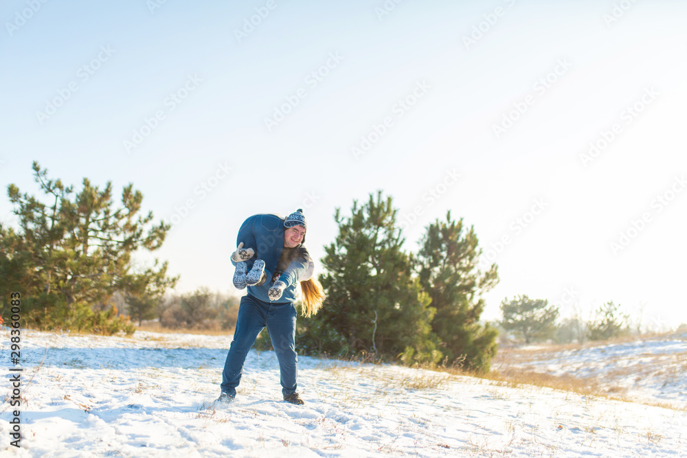 Loving couple play in the winter in the forest. The guy threw the girl on his back and runs with her through the forest. Laugh and have a good time.
