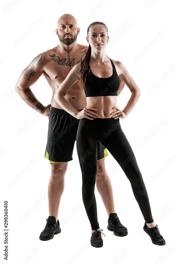 Athletic man in black shorts and sneakers with brunette woman in leggings and top posing isolated on white background. Fitness couple, gym concept. Athletic man in black shorts and sneakers with brunette woman in leggings and top posing isolated on white background. Fitness couple, gym concept.