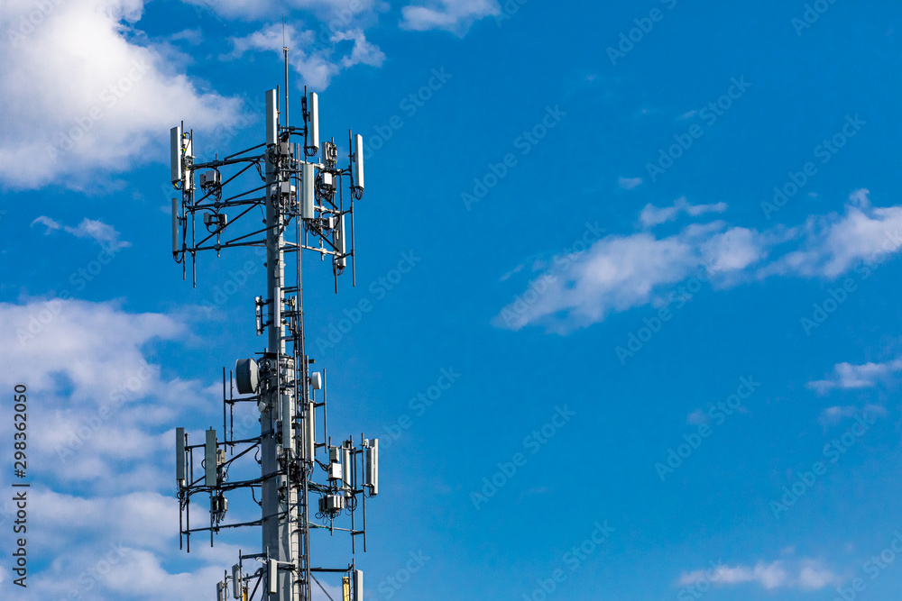 A low angle view of a typical cell network antenna tower. Used to send and receive mobile network communications, with copy-space and cloudy blue sky. A low angle view of a typical cell network antenna tower. Used to send and receive mobile network communications, with copy-space and cloudy blue sky.