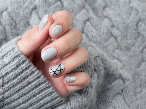 Females hand in gray knitted sweater with modern manicure close up