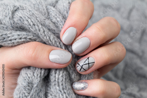 Females hand with modern manicure holds gray knitted sweater  close up