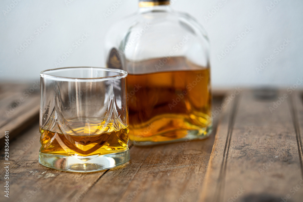 Glass and bottle of golden shimmering whisky on wooden table Glass and bottle of golden shimmering whisky on wooden table