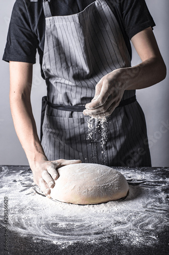Posypywanie mąką chleba lub ciasta przez kucharza na ciemnym stole