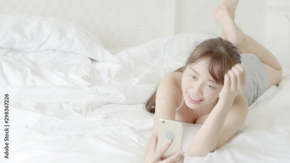 Beautiful portrait young asian woman lying taking a selfie with smart mobile phone on bedroom in the morning at home, girl is photographing happy and smile with fun, lifestyle concept, slow motion. Beautiful portrait young asian woman lying taking a selfie with smart mobile phone on bedroom in the morning at home, girl is photographing happy and smile with fun, lifestyle concept, slow motion.