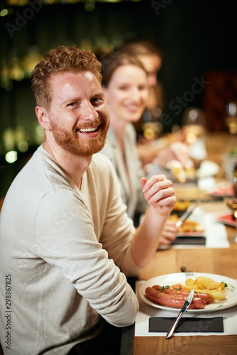 Handsome caucasian bearded ginger sitting in restaurant with his friends and having dinner.