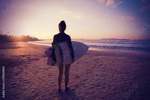 Woman surfer with surfboard ready to surf on sunrise beach