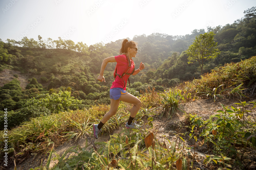 Woman ultramarathon runner running up on mountain slope in tropical forest