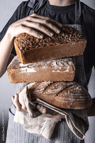 Trzymanie różnych rodzajów chleba w dłoniach na szarym tle w stylu rustykalnym przez osobę w fartuchu