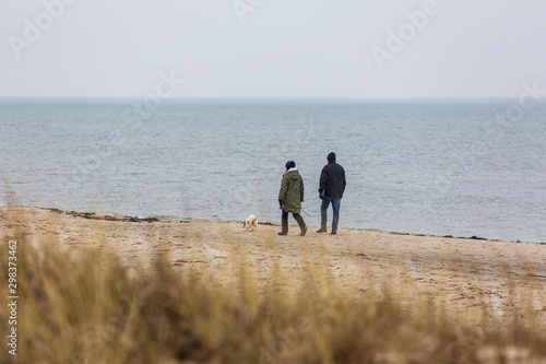A couple with a dog is walking on a beach on a cold winter day