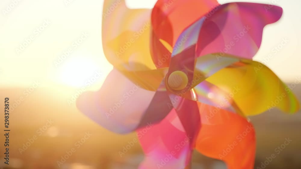 A rotate colored plastic pinwheel with a blowing wind stands on sand by the sea against the smooth surface of the sea and a bright pink sunset. Toy mill on the beach. Large disk of the sun. Copyspace A rotate colored plastic pinwheel with a blowing wind stands on sand by the sea against the smooth surface of the sea and a bright pink sunset. Toy mill on the beach. Large disk of the sun. Copyspace
