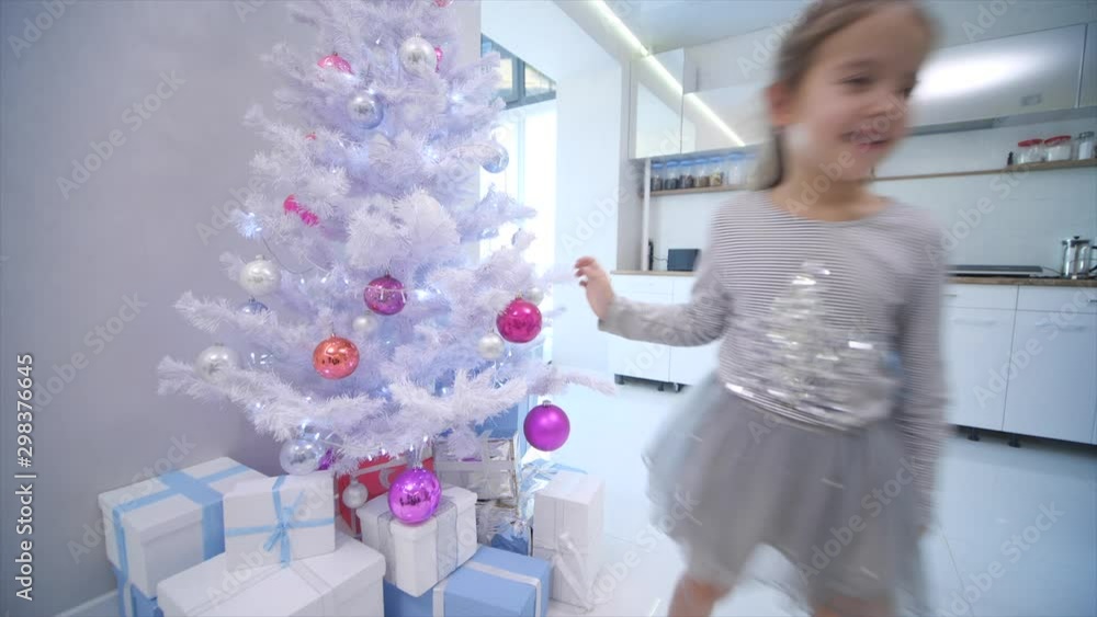 Pretty little girl comming to the christmas tree on the forefront and puts a glass bauble on one of the branches. Pretty little girl comming to the christmas tree on the forefront and puts a glass bauble on one of the branches.