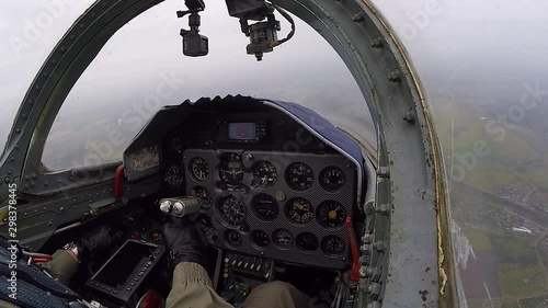 The hand of pilot hold and control helm. Gray training fighter plane make triple barrel roll maneuver against a cloudy sky. Aircraft performs rotates 360 °. View of cockpit and dashboard close up.