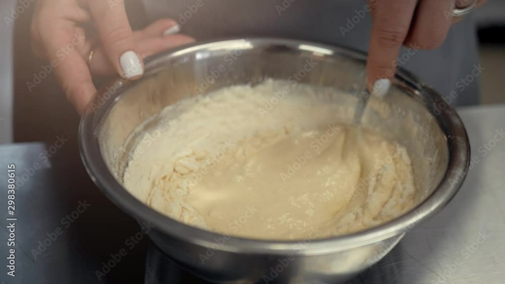 Kneading the dough with a whisk. Female hands mix the dough in an iron plate Kneading the dough with a whisk. Female hands mix the dough in an iron plate