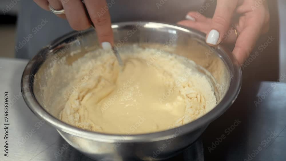 Kneading the dough with a whisk. Female hands mix the dough in an iron plate Kneading the dough with a whisk. Female hands mix the dough in an iron plate