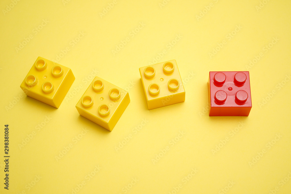 A yellow children's plastic bricks or blocks toy with a unique red color on yellow background A yellow children's plastic bricks or blocks toy with a unique red color on yellow background