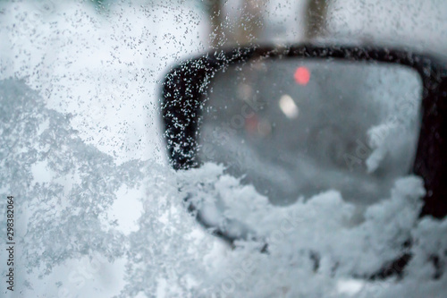 The side window of the car is covered with snow and ice, the rear view mirror in the background. The view from the car. Bokeh. Art. Concept. Winter, daytime.