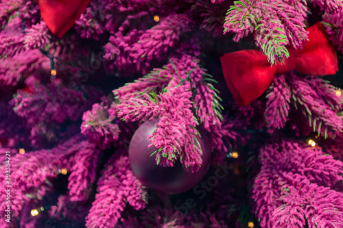 Christmas decorations. Purple branches of Xmas tree, decorated with red bows and purple Christmas toys. Close-up