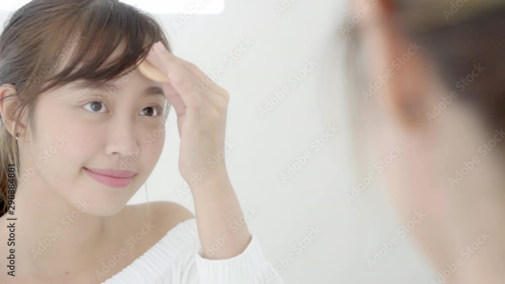 Portrait beautiful young asian woman applying powder puff at cheek makeup of cosmetic looking mirror, lifestyle of beauty girl with skin face smile in the bedroom, health and wellness concept. Portrait beautiful young asian woman applying powder puff at cheek makeup of cosmetic looking mirror, lifestyle of beauty girl with skin face smile in the bedroom, health and wellness concept.