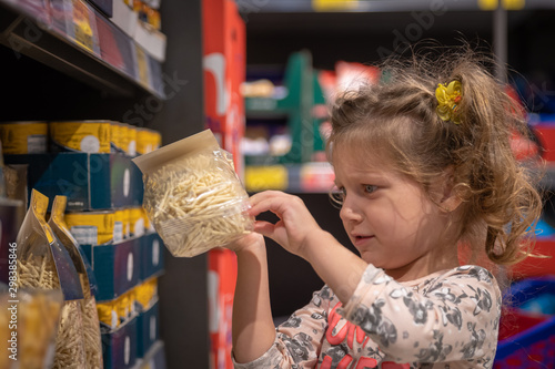 little girl is picking a pack of pasta in a supermarket