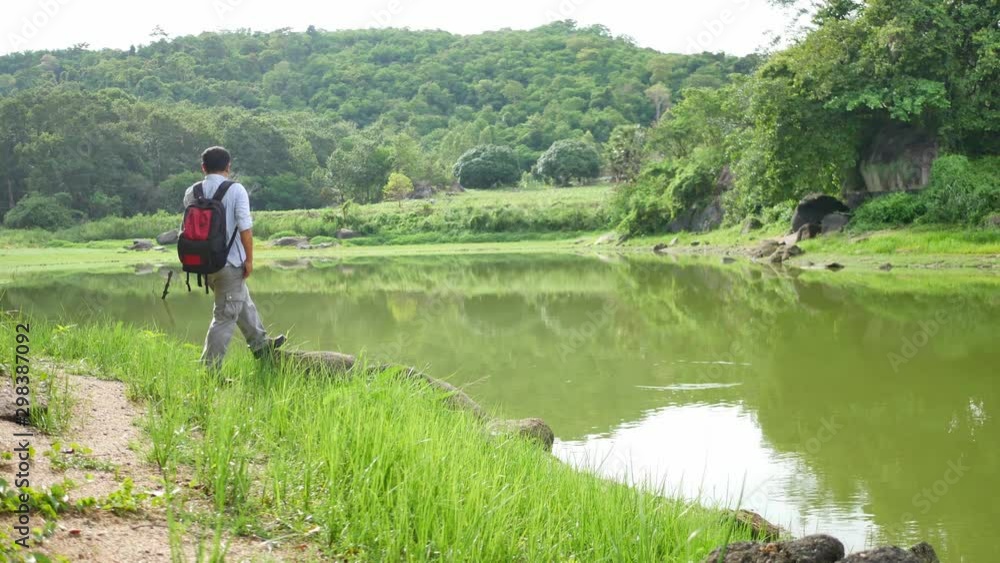 An adventurous man feels peace and relaxing to walks alone in the forest during holiday time. Green mountain and pond on the background. Nature and Travel concept
