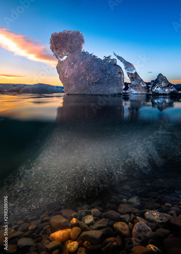 Underwater picture of small iceberg in Jokulsarlon Galcier Lagoon reflected in calm water at sunset, showing underwater details and colorful sky above. photo