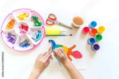 Hands of a child make a chameleon from cardboard. Rainbow color