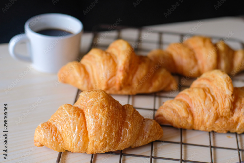 Tasty fresh croissants on cooling rack with white cup of coffee on black background. Tasty fresh croissants on cooling rack with white cup of coffee on black background.