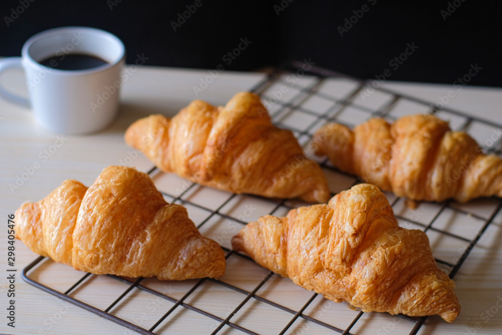 Tasty fresh croissants on cooling rack with white cup of coffee on black background.