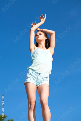 Young beautiful woman in a turquoise blouse posing against the blue sky