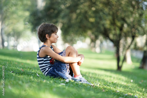 Little girl, eight years old, sitting on the grass outdoors.