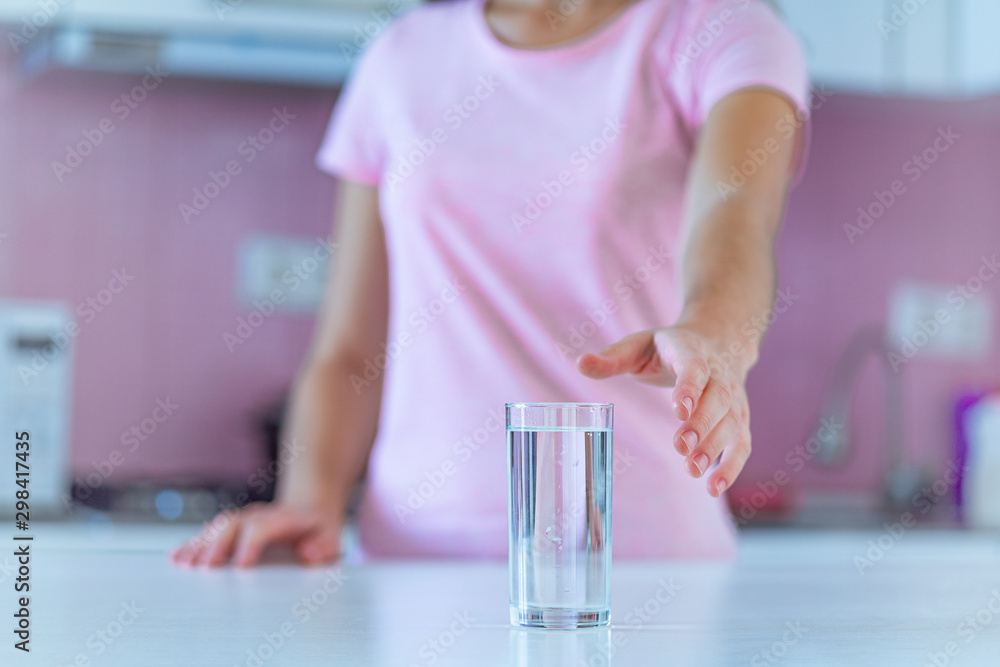 Fototapeta premium Woman with a glass of clear purified water in the kitchen at home. Healthy lifestyle