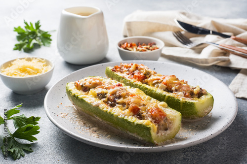 Baked stuffed zucchini boats with minced chicken mushrooms and vegetables with cheese on a plate.