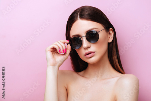 Portrait of an attractive young girl in round glasses on a pink background in studio