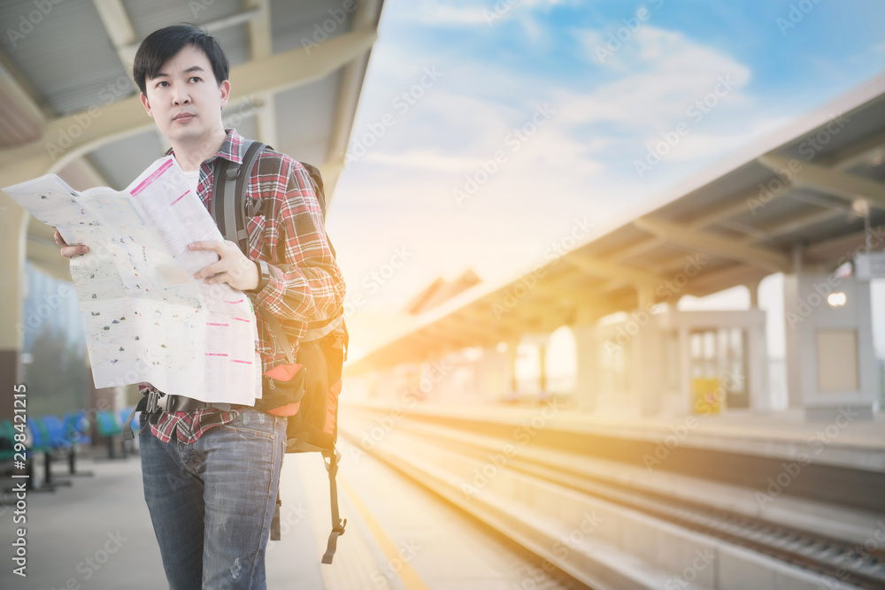 Young asian traveling backpacker wearing a red plaid shirt, sunglasses and looking a paper map at train station. Vintage tone. Travel concept. Young asian traveling backpacker wearing a red plaid shirt, sunglasses and looking a paper map at train station. Vintage tone. Travel concept.