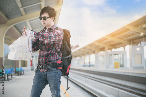 Men wearing a red plaid shirt and standing waiting for the train at train station. 