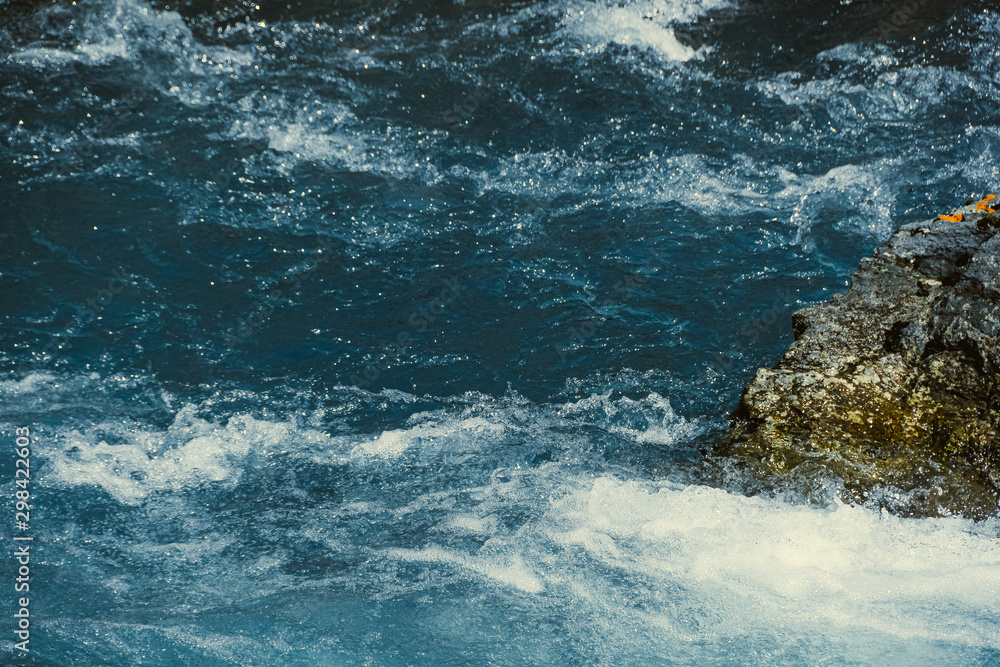 Mountain river with stone in blue water. Turquoise waves of sea tide